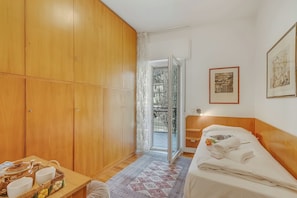 A room with a bed, a wooden wardrobe, a table with bowls and a kettle, and a door leading to an outdoor area. - Rosa Apartment, Balcony and AC (Riva del Garda)