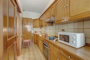 A kitchen with wooden cabinets, a microwave, a sink, and a chair. - Rosa Apartment, Balcony and AC (Riva del Garda)