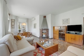 A living room with a sofa, coffee table, fireplace, TV, and wooden cabinet. - Rosa Apartment, Balcony and AC (Riva del Garda)