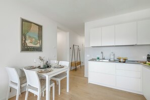 A modern kitchen with white cabinetry, a dining table with chairs, and a hanging chair. - Bella Vista Apartment (Riva del Garda)