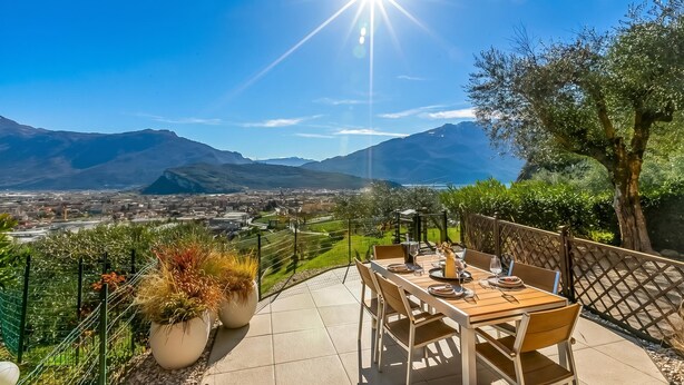 A patio with a table set for dining, surrounded by a fence and potted plants, overlooking a valley and mountains. - Bella Vista Apartment (Riva del Garda)