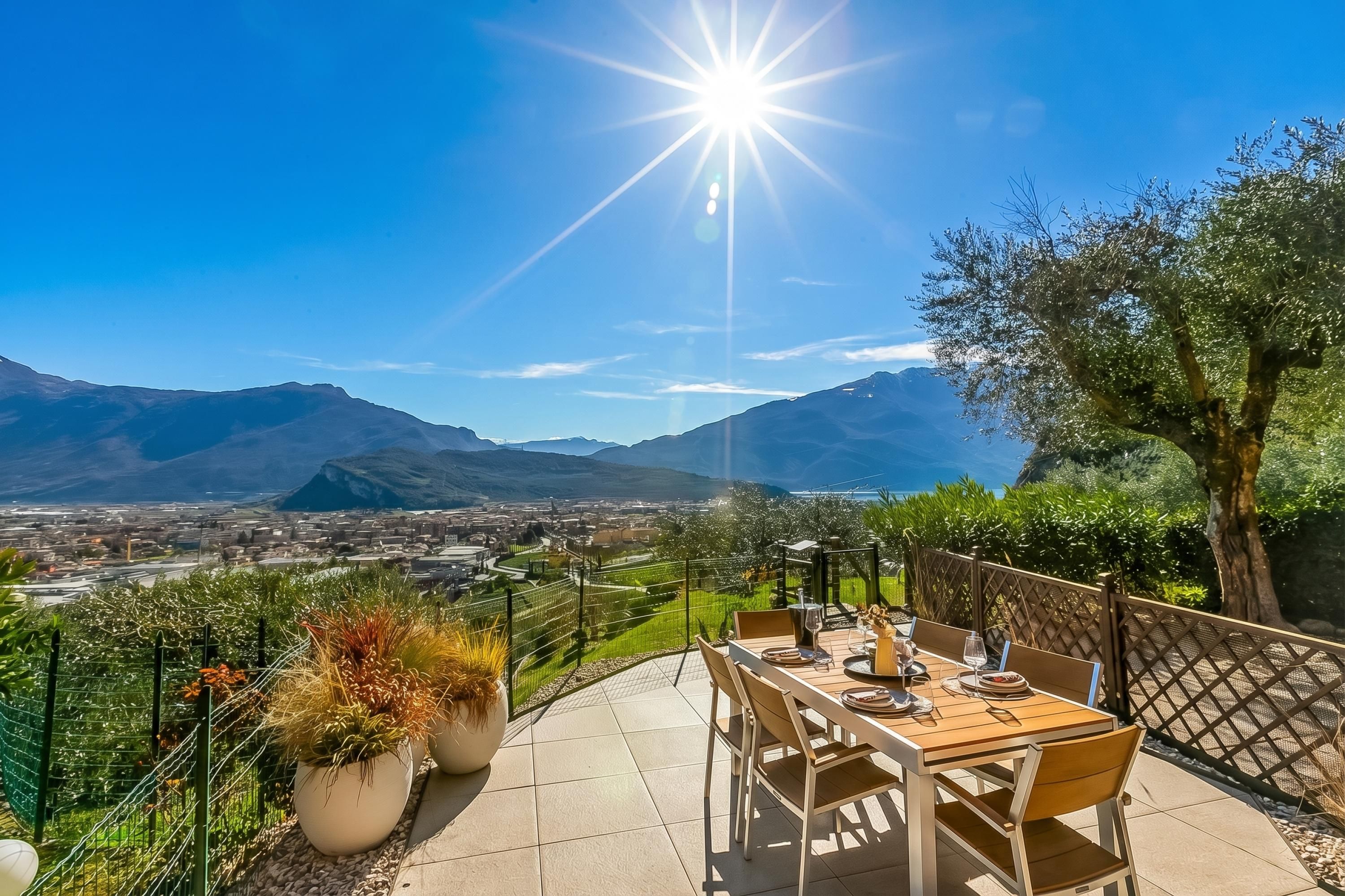 Un patio con tavolo apparecchiato per mangiare, circondato da una recinzione e piante in vaso, con vista su una valle e montagne.