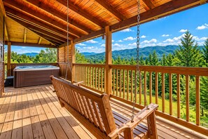 A wooden deck with a hot tub and a swing, overlooking a mountainous landscape. - Honey Bear | 1,890 Sq Ft · Mountain Views · Pool Table · Sleeps 9 (Sevierville)