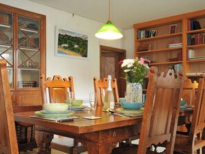 Ein Essbereich mit einem Holztisch, Stühlen, einer Vase mit Blumen und Bücherregalen.