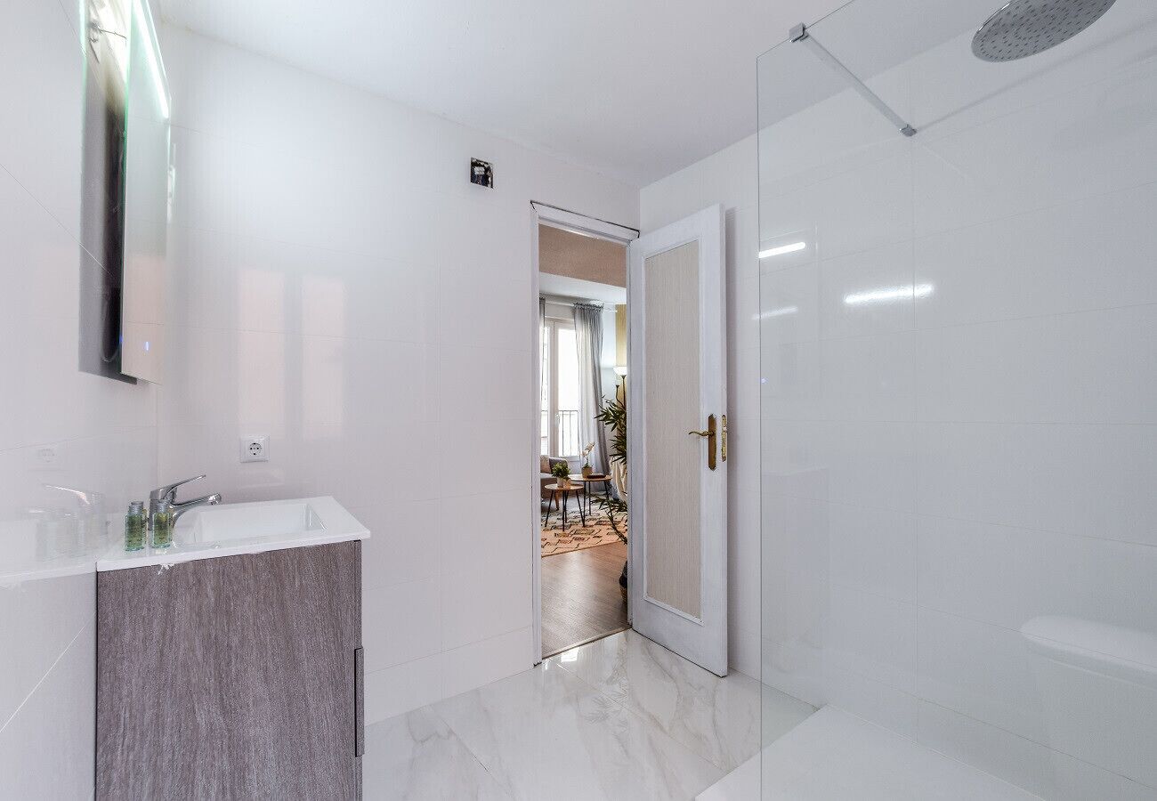A modern bathroom with a white vanity, a shower area, and a visible doorway leading to a living space.
