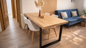 Uma sala de estar moderna com uma mesa de jantar de madeira, cadeiras brancas, um sofá azul e uma pequena mesa lateral com uma planta.