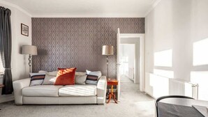 Een moderne woonkamer met een bank, lampen en behang met een patroon.