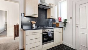Een moderne keuken met lichte houtkleurige kastjes, een zwart aanrecht, een roestvrijstalen afzuigkap en een inbouwoven.