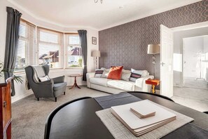 A modern living room with a sofa, armchair, and a dining table with a book. - Coorie Doon, Largs, spacious 2 bedroom apartment (North Ayrshire Council)
