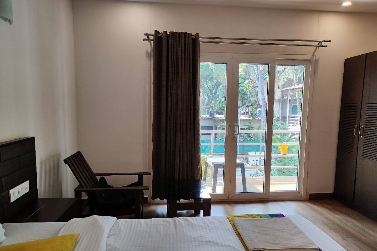 A hotel room with a bed, a chair, a desk, a wardrobe, and a sliding glass door leading to an outdoor area.