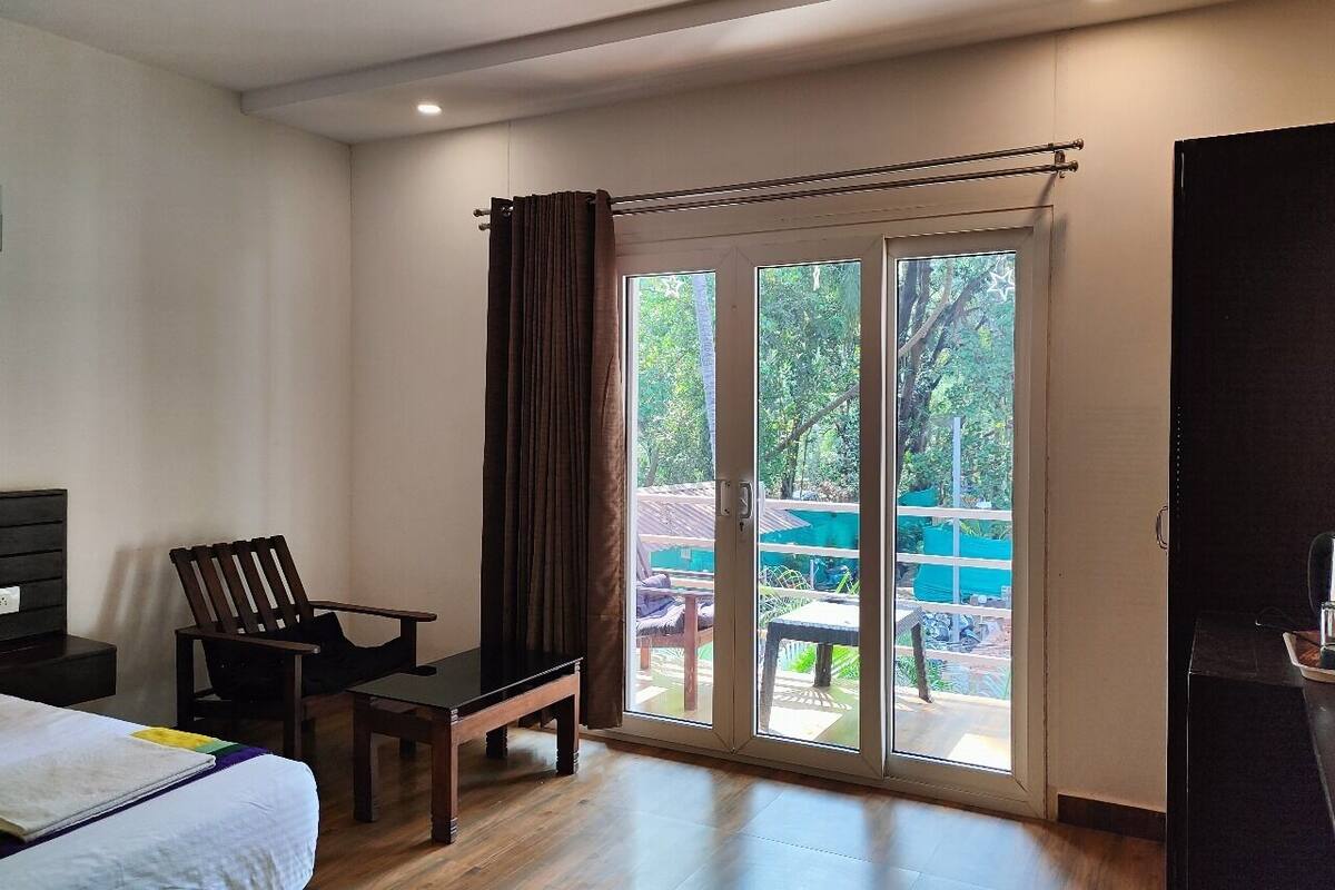 A hotel room with a bed, a desk, a chair, and a sliding glass door leading to an outdoor area with a table and chairs.