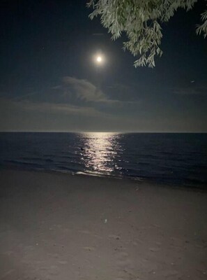 Ein Strand bei Nacht mit einem deutlich sichtbaren Mondspiegel auf dem Wasser.