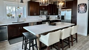 A modern kitchen with dark wooden cabinets, stainless steel appliances, and a large island with bar stools. - Waterfront Beach House - Deck, BBQ & Private Beach (Selkirk)