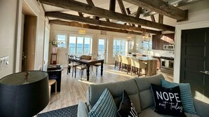 A spacious living area with a high ceiling, exposed wooden beams, a dining area, and a kitchen. - Waterfront Beach House - Deck, BBQ & Private Beach (Selkirk)