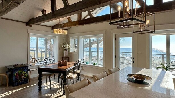 A spacious kitchen with a large island, wooden beams, and large windows overlooking the beach. - Waterfront Beach House - Deck, BBQ & Private Beach (Selkirk)