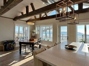 A spacious kitchen with a large island, wooden beams, and large windows overlooking the beach. - Waterfront Beach House - Deck, BBQ & Private Beach (Selkirk)
