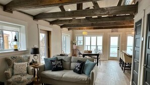A cozy living room with a sofa, armchair, and a dining area with a table and chairs. - Waterfront Beach House - Deck, BBQ & Private Beach (Selkirk)