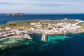 Uma cidade costeira com um porto de recreio, edifícios brancos e uma fortaleza numa colina.