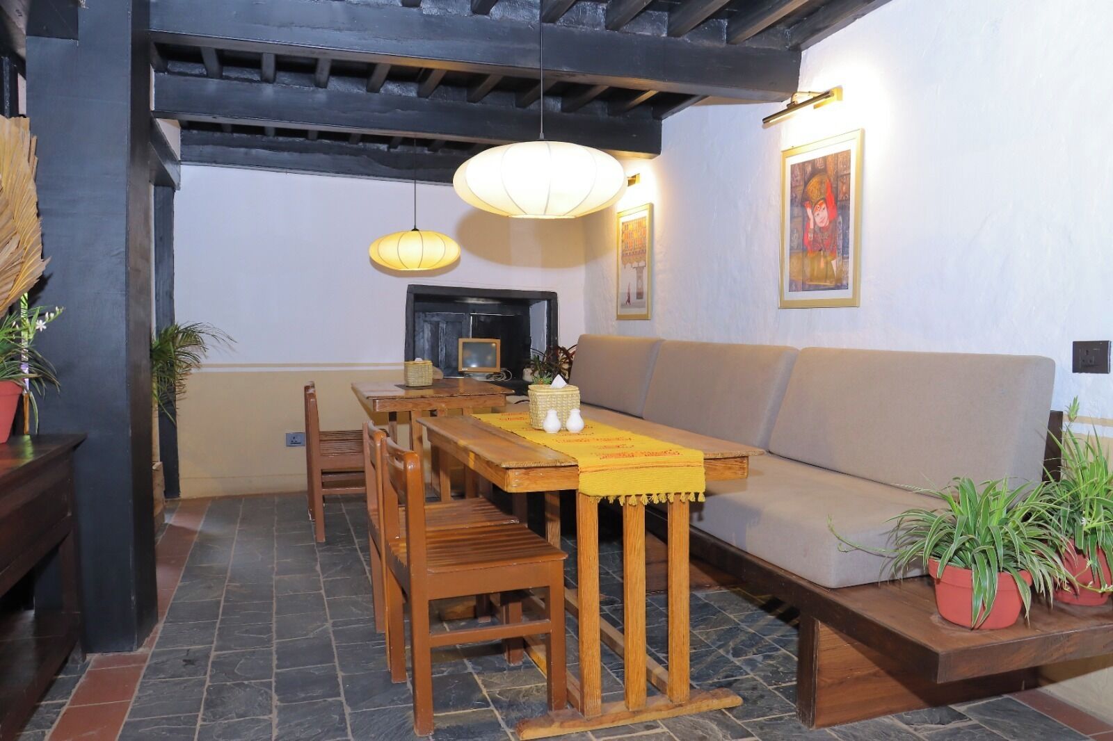 A dining area with a wooden table, chairs, a sofa, and potted plants.