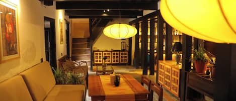 A dining area with a wooden table, chairs, a sofa, and a staircase in the background.