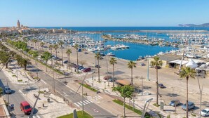 A marina with boats, a clear sky, and a road with palm trees. - Sunset Harbor Penthouse with a sun-drenched panoramic terrace and garage (Alghero)