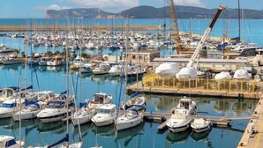 A marina with numerous boats docked, a crane, and a clear view of the sea and distant mountains. - Sunset Harbor Penthouse with a sun-drenched panoramic terrace and garage (Alghero)
