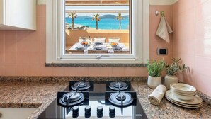 A kitchen with a gas stove, a window with a view of the sea, and a towel hanging on the wall. - Sunset Harbor Penthouse with a sun-drenched panoramic terrace and garage (Alghero)