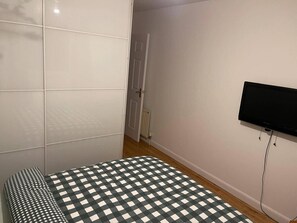 A bedroom with a checkered bedspread, a television mounted on the wall, and a door leading to another room. - Charming Aberdeen Apartment (Aberdeen)
