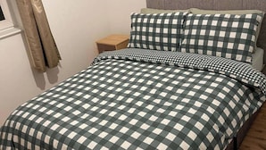 Een bed met een geruit beddegoed, een houten nachtkastje en een grijs hoofdeinde.