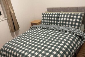 Una cama con una colcha a cuadros, una mesita de noche de madera y un cabecero gris.