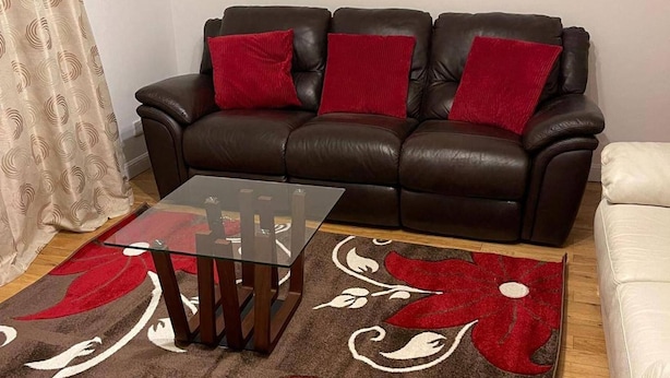 Een woonkamer met een bruine leren bank, een glazen salontafel en een kamerkleed met een patroon.