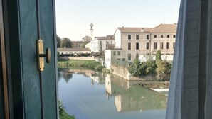 A view of a calm river with buildings and a tower in the background. - La Finestra sul Fiume - 5 min from the Basilica (Vicenza)