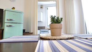 A kitchen with a vintage teal refrigerator, a clock on the wall, a potted plant on the counter, and a striped tablecloth. - La Finestra sul Fiume - 5 min from the Basilica (Vicenza)