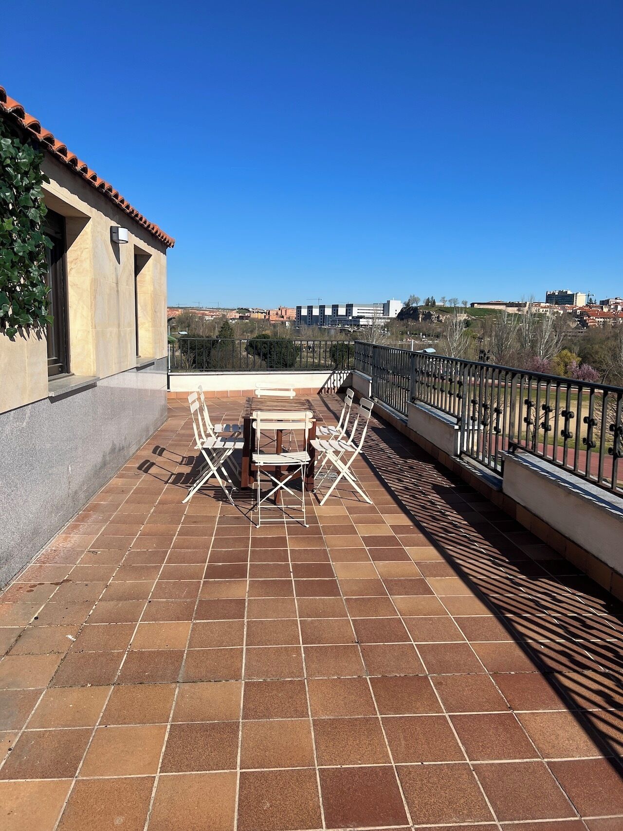 Eine Terrasse mit Tisch, Stühlen, Geländer und Blick auf die Stadt.