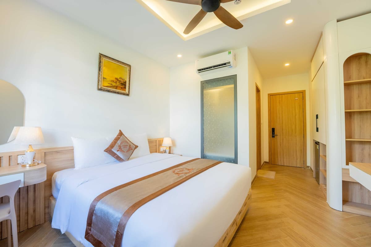 A hotel room with a bed, desk, chair, ceiling fan, and a door leading to another room.