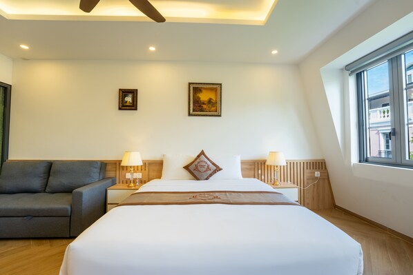 A hotel room with a bed, a sofa, two wall-mounted lamps, a ceiling fan, and a window. - Harmony Phu Quoc (Phu Quoc)
