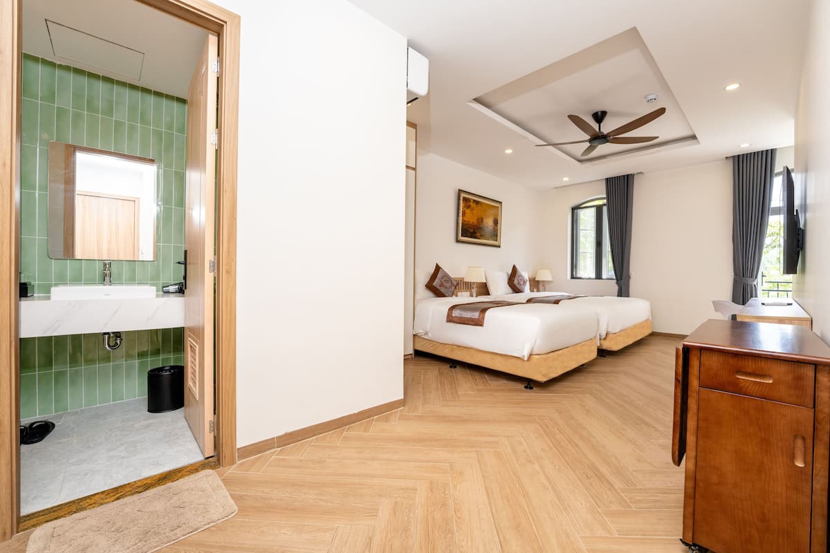 A hotel room with a wooden floor, a bed, a desk, a mirror, and a ceiling fan.