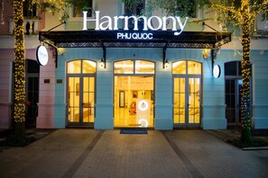En hotellentrén med en skylt som visar texten ”Harmony PHUQUOC”, med en inbjudande valvformad ingång och upplysta fönster.