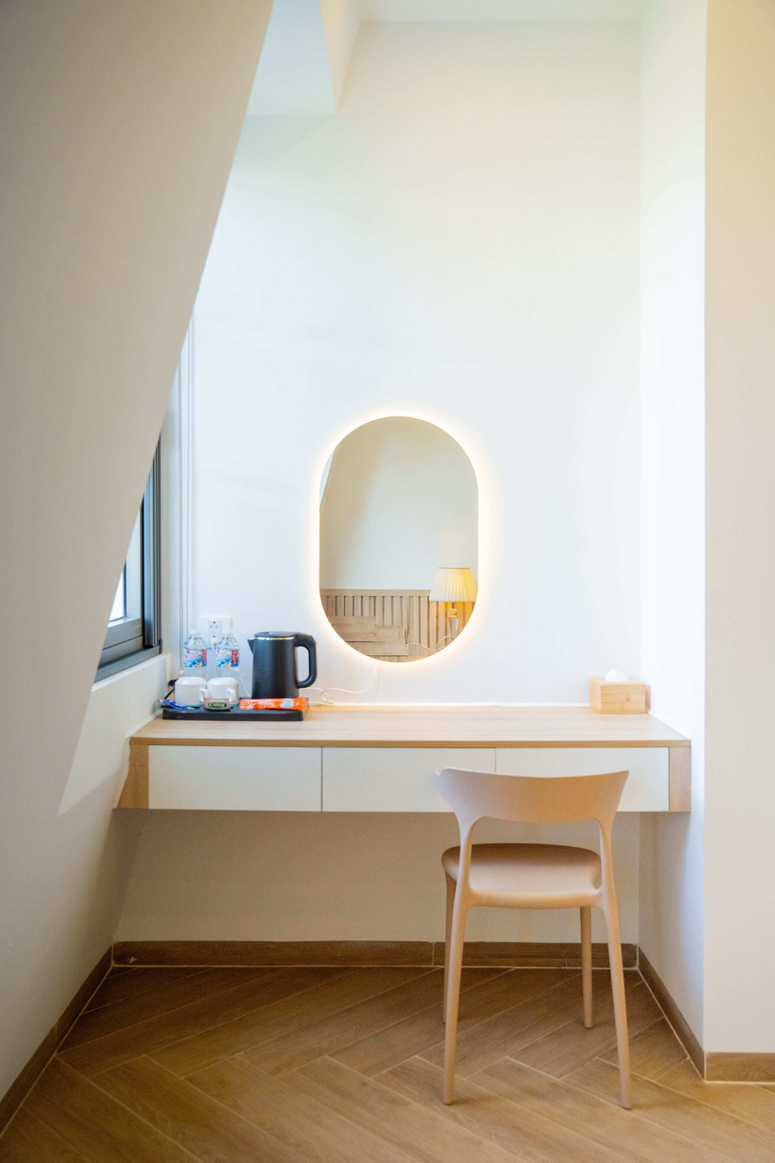 A modern room with a wooden desk, a chair, a coffee maker, and a mirror with a light.