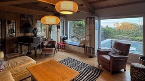 A cozy living room with a piano, a sofa, a coffee table, and a view of the outdoors. - Starboard Sunset – Coastal Views, Hot Tub & Private Retreat (Bodega Bay)