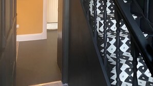 Un escalier dont la rampe présente un motif géométrique, menant à une pièce dotée d’une porte et d’un tableau encadré accroché au mur.