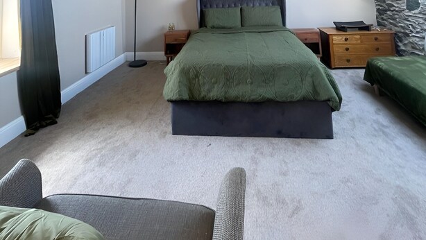 Une chambre avec un plafond en pente, un lit recouvert d’une couverture verte, une table de chevet, une commode et un mur d’accent en pierre.