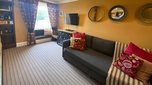 Un salon avec un canapé, un téléviseur, une bibliothèque et une fenêtre avec des rideaux.