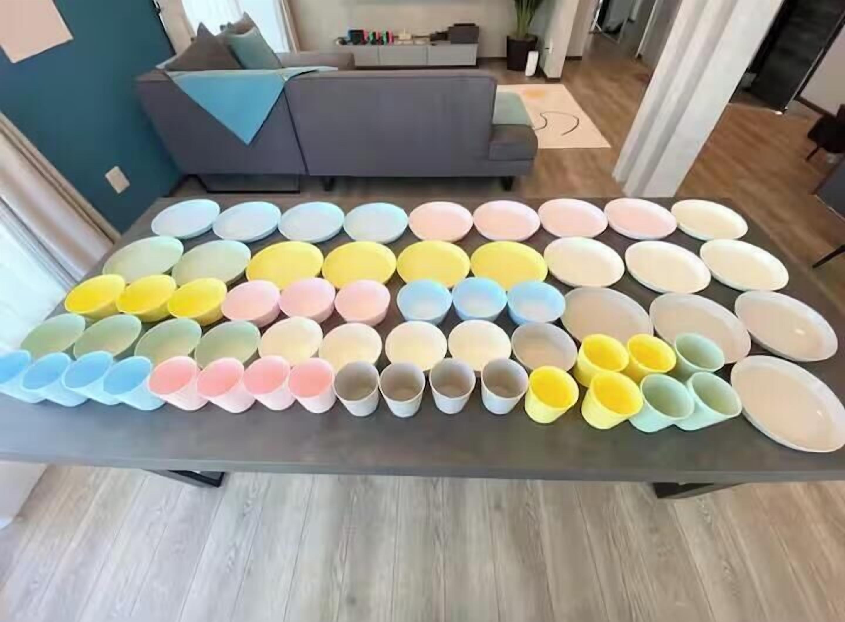 A room with a large table displaying a variety of colorful cups.