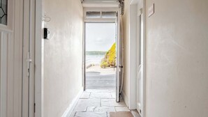 Un couloir avec un sol en pierre, une porte donnant sur l’extérieur et une vue sur une plage.