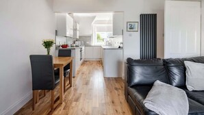 Un salon moderne avec un canapé en cuir noir, une table à manger en bois et une cuisine en arrière-plan.