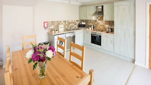 A modern kitchen with white cabinets, a microwave, stove, and a dining area with a wooden table and chairs. - Simmental Cottage Daviot (Inverness)