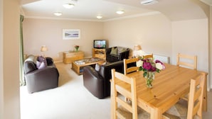 A living room with a sofa, a wooden table, a television, and a vase with flowers. - Simmental Cottage Daviot (Inverness)