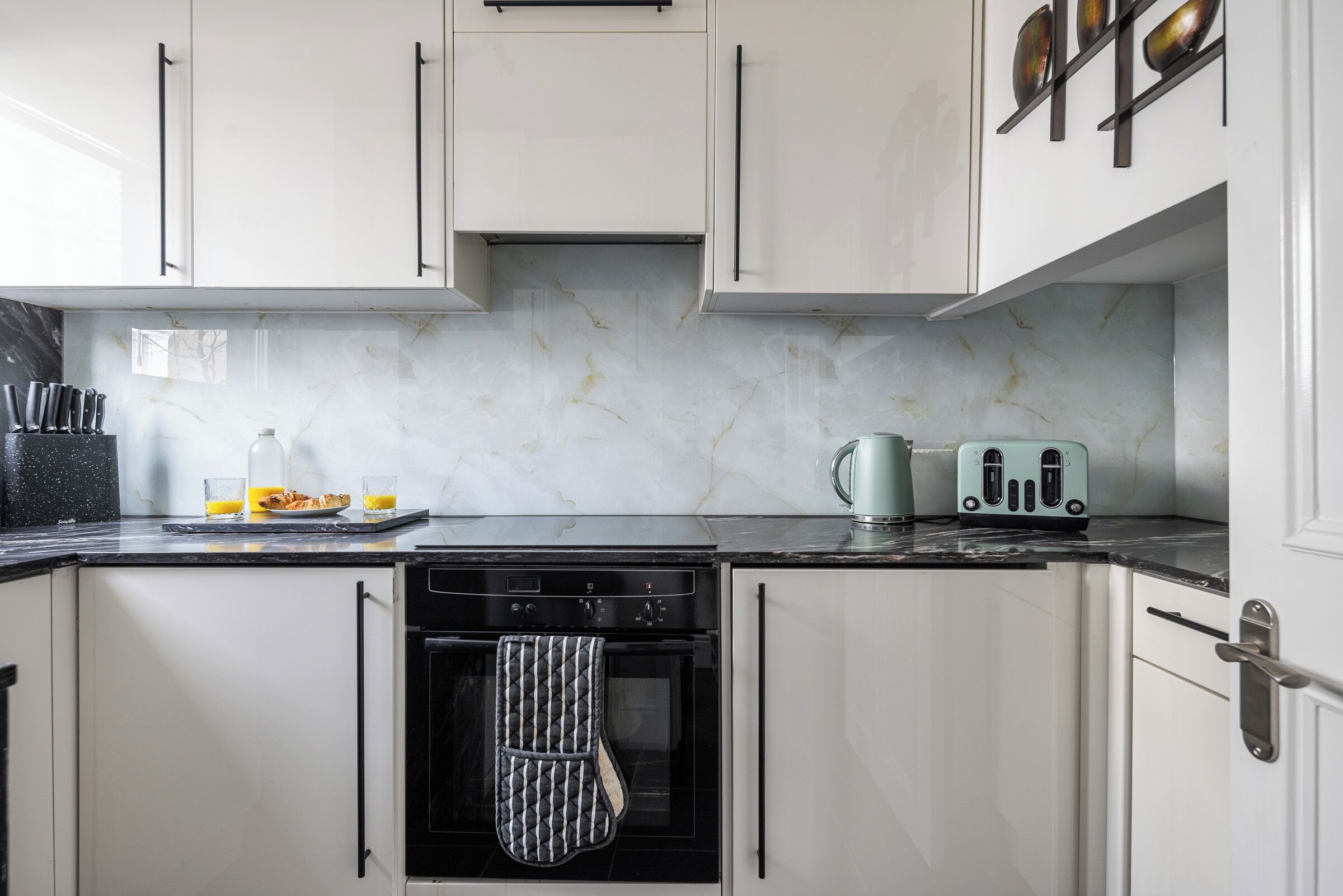 A kitchen with white cabinets, a black oven, a kettle, and a toaster.