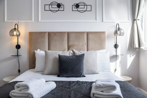 A neatly made bed with a dark quilt, white pillows, and a single dark pillow. There are two wall-mounted lamps on either side of the bed. - Authentic Duplex Apt and Private Parking in Chelsea (London)